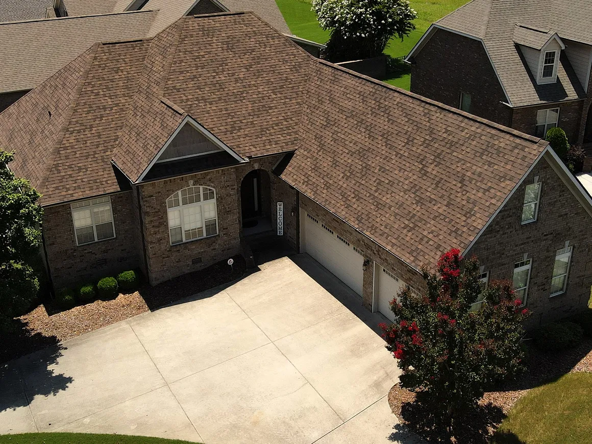 Aerial view of a brick home with brown multi-gable roof and two-car garage